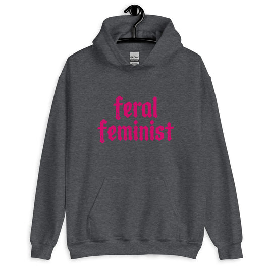 A charcoal grey hoodie with hot pink graphic that says ' Feral Feminist’ hanging on a hanger rewilding by Rebel Girl Rampage