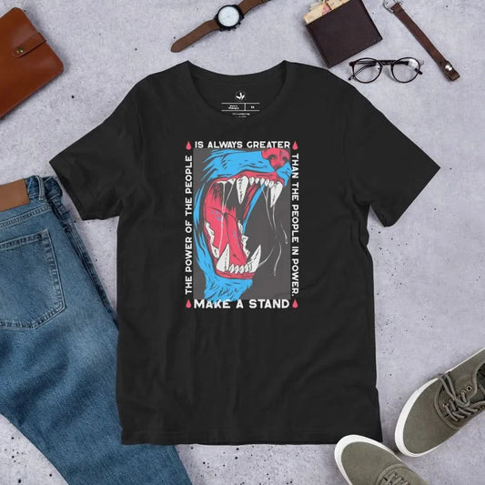 A black unisex t-shirt with a graphic design featuring a wolf’s mouth, with red and blue accents, and text that reads 'The power of the people is always greater than the people in power. MAKE A STAND’. by Raphael Warnock. Rebel Girl Rampage