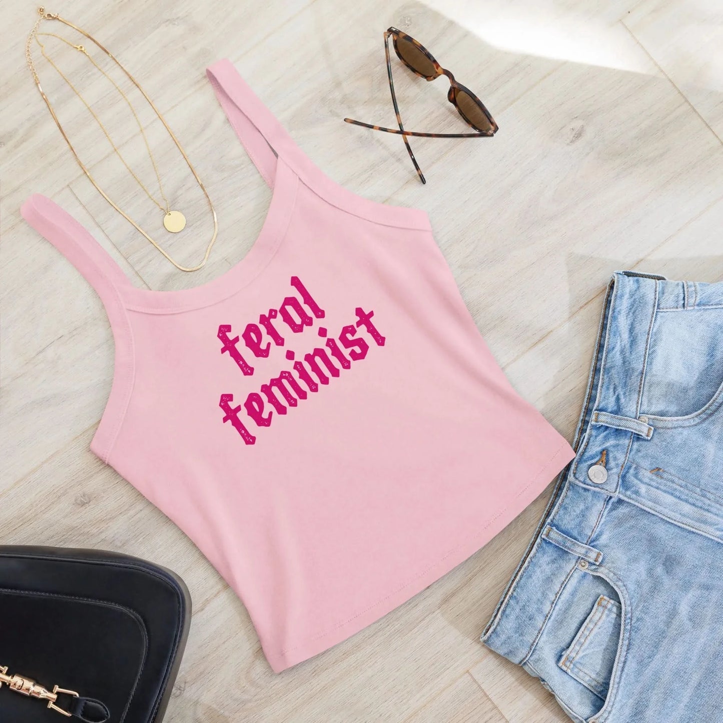 Feral Feminist pink crop tank top with barbie pink writing styled with jeans on the floor by Rebel Girl Rampage