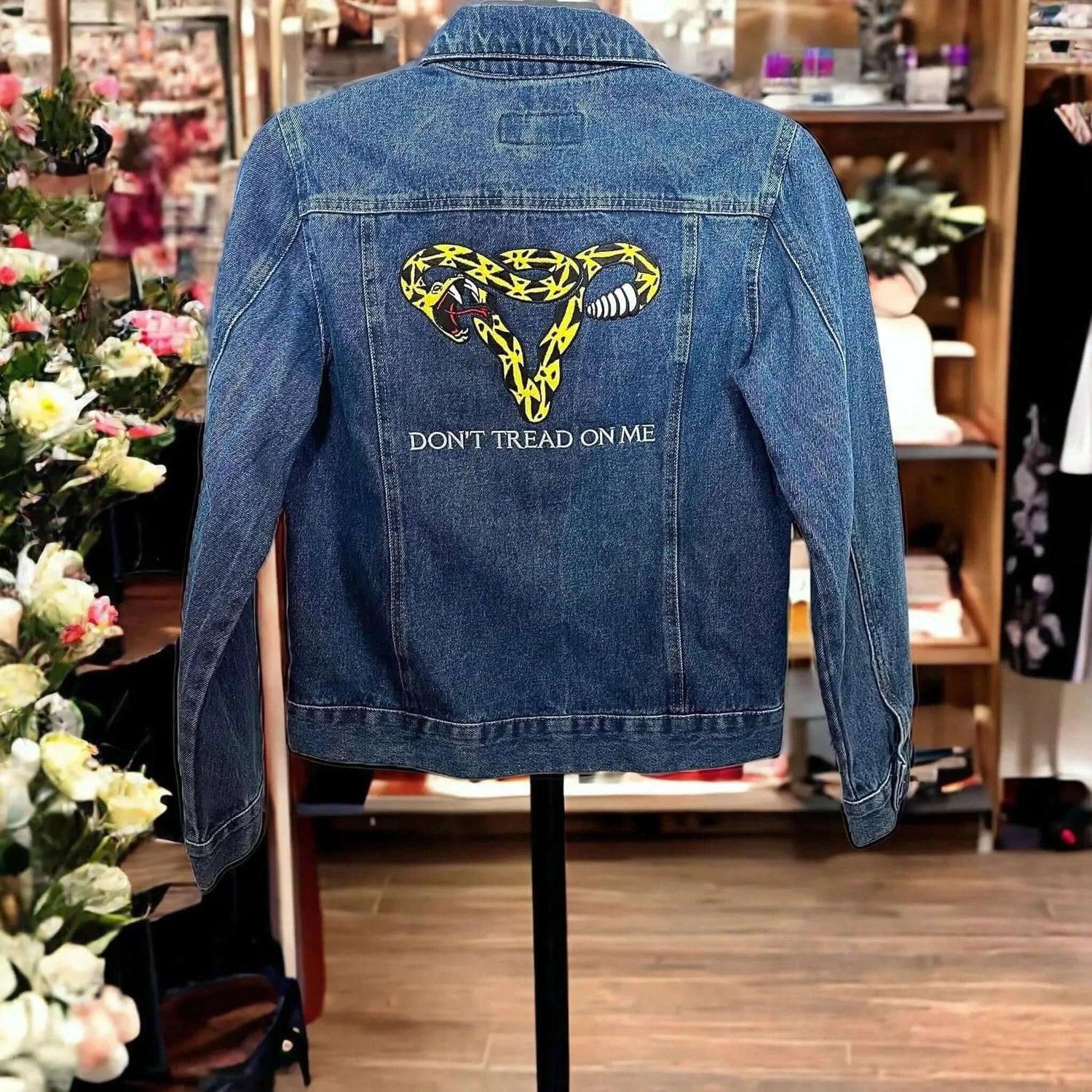 Blue denim jacket hangin in a ship with a Don’t Tread On Me Uterus rattlesnake embroidered on the back at Rebel Girl Rampage 