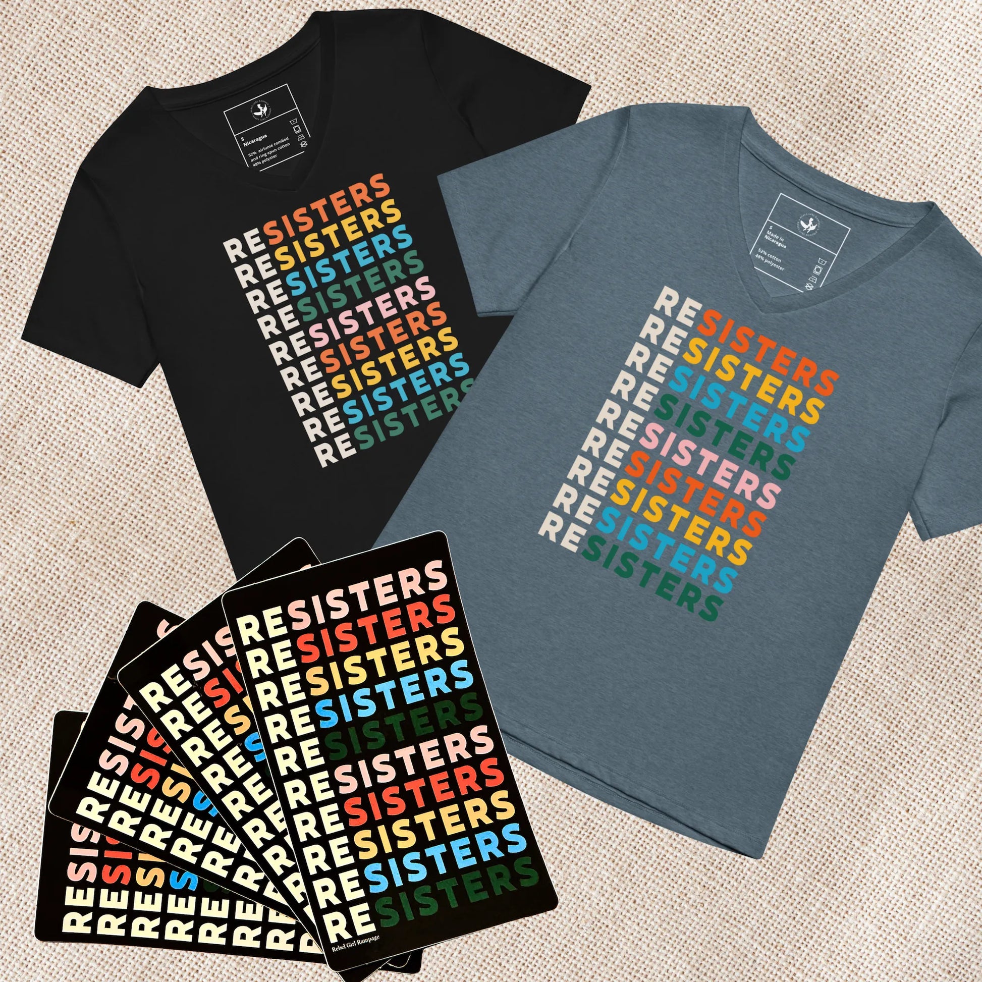 Black and blue women’s v neck t-shirts with 'RESISTERS' text in multicolor on a textured surface with 4 stickers for a feminist holiday sisterhood gift bundle, Anne Lesniak, Rebel Girl Rampage 